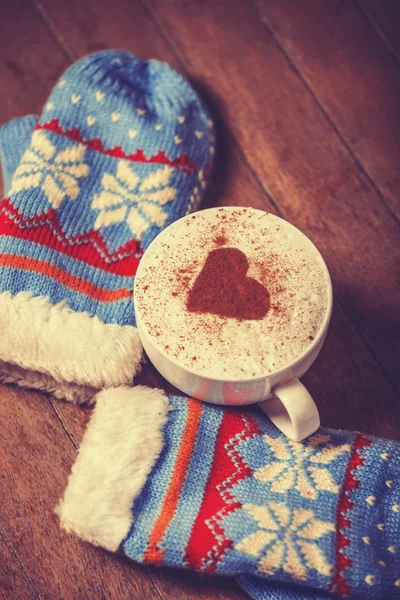 Gloves and cup with coffee and shape of the cacao heart on it. — Stock Photo, Image