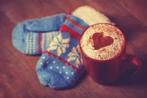 Gloves and cup with coffee and shape of the cacao heart on it. — Stock Photo, Image