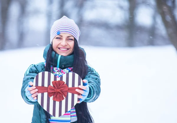 Menina morena bonita com caixa de forma de coração no parque de inverno . — Fotografia de Stock