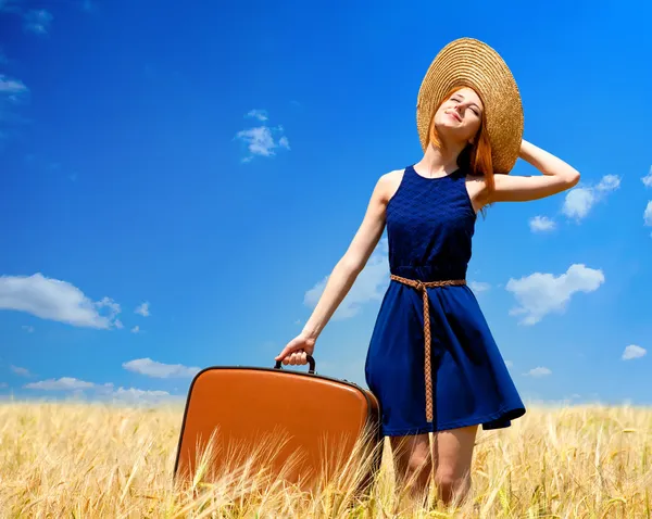 Rothaarige Mädchen mit Koffer im Frühlingsweizenfeld. — Stockfoto