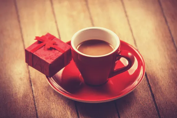 Red cup of the coffee and little gift. — Stock Photo, Image