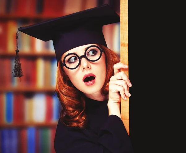 Graduating student girl in an academic gown near blackboard — Stock Photo, Image