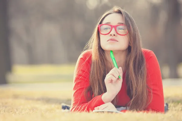 Ragazza adolescente con una penna sdraiata su un'erba . — Foto Stock