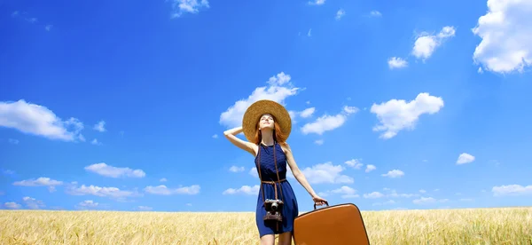 Redhead girl with suitcase at spring wheat field. — Stock Photo, Image