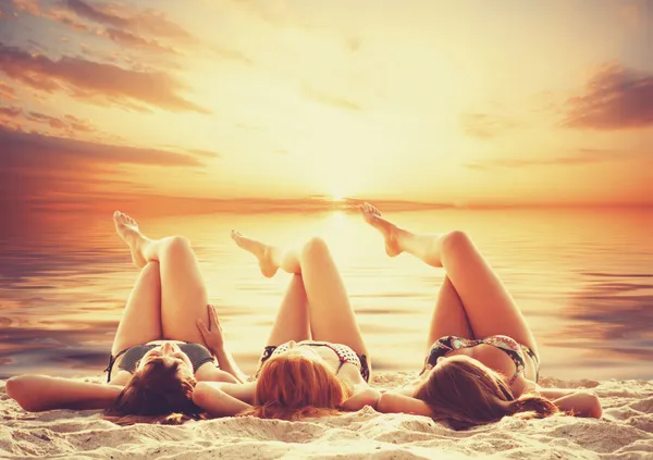 Drie meisjes op het strand in zonsondergang. — Stockfoto