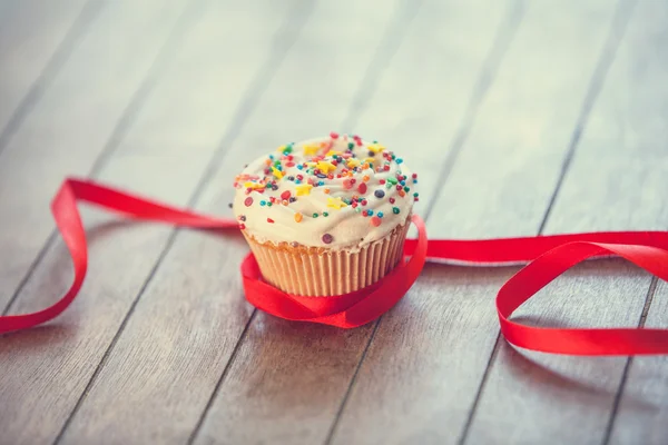 Cupcake and bow on wooden table. — Stock Photo, Image