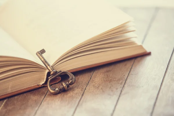 Retro key and opened book on wooden table. — Stock Photo, Image