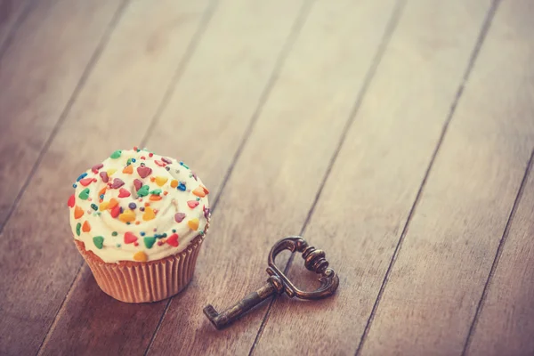 Cupcake and key on wooden table. — Stock Photo, Image