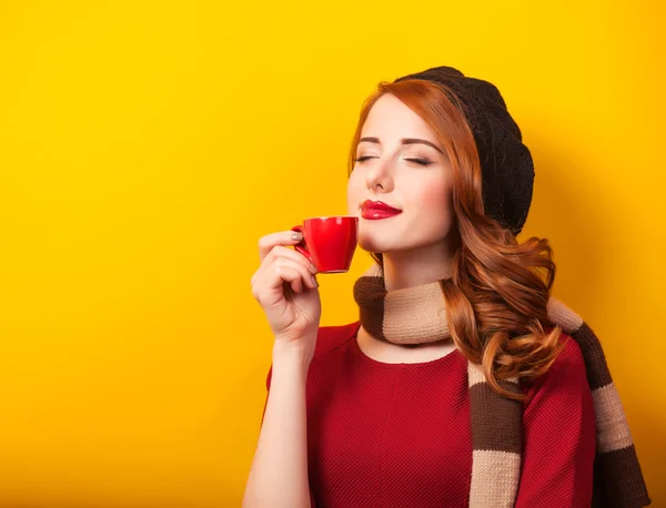 Roodharige meisje met rode kopje koffie of thee op gele achtergrond. — Stockfoto
