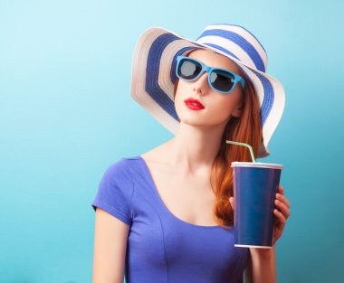 Kızıl saçlı kız içki ve mavi arka plan üzerinde güneş gözlüğü