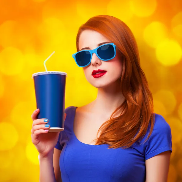 Menina ruiva com bebida e óculos de sol no fundo amarelo — Fotografia de Stock