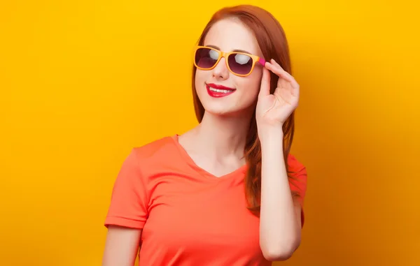 Joyeux rousse fille en lunettes de soleil sur fond jaune — Photo