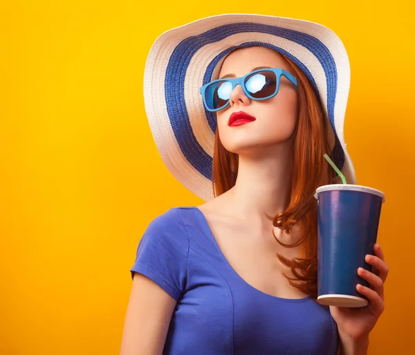 Κοκκινομάλλα κοπέλα με ποτό και γυαλιά ηλίου σε κίτρινο φόντο — Φωτογραφία Αρχείου
