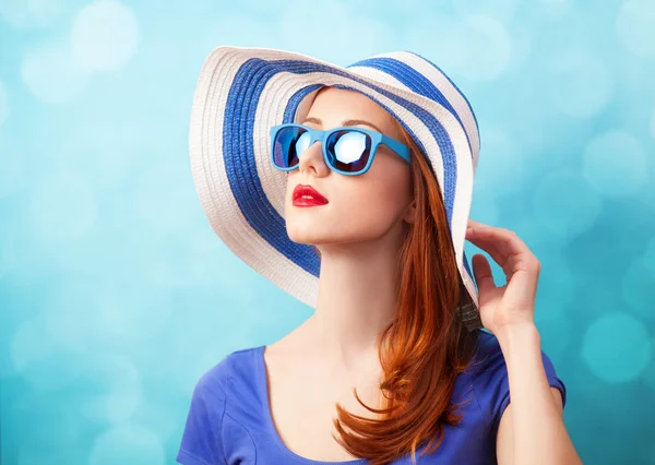 Pelirroja con gafas de sol y sombrero sobre fondo azul . — Foto de Stock