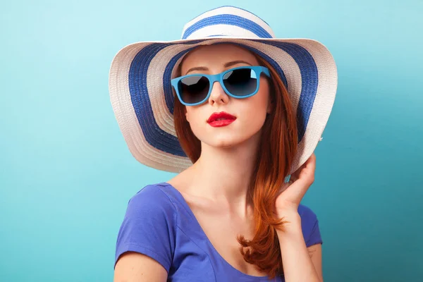 Redhead girl with sunglasses and hat on blue background. — Stock Photo, Image