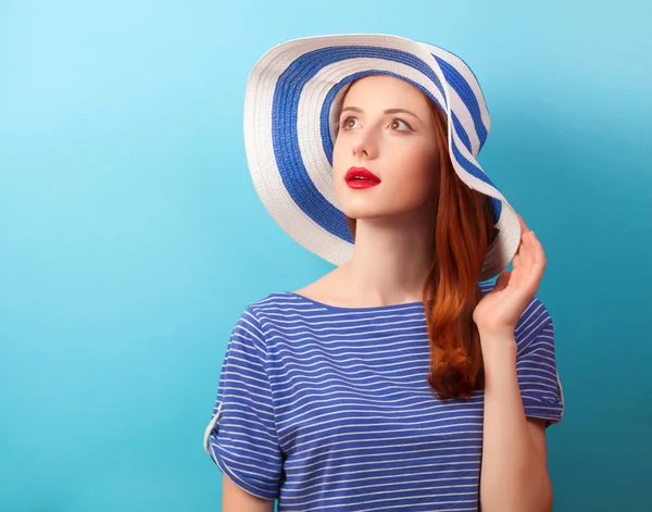 Roodharige meisje in hoed op blauwe achtergrond. — Stockfoto