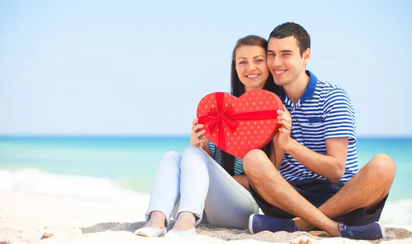 Jovem casal com presente na praia no dia de verão . — Fotografia de Stock