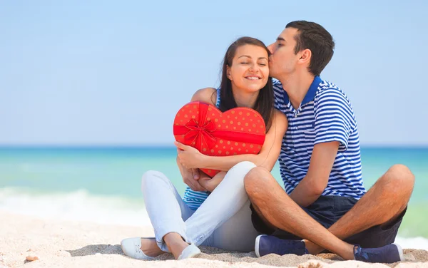Young couple with gift on the beach in summer day. — Stock Photo, Image