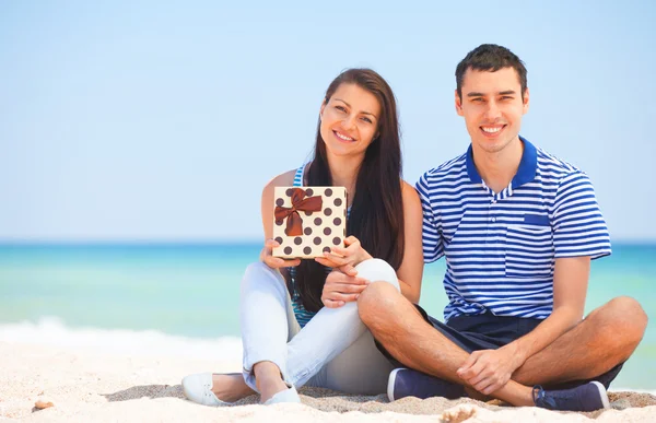 Young couple with gift on the beach in summer day. — Stock Photo, Image