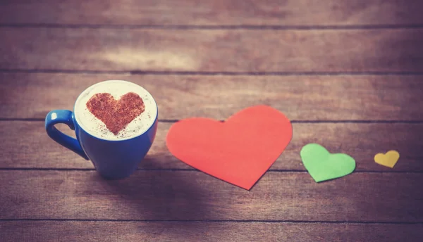 Tasse mit Kaffee- und Herzpapier auf Holztisch. — Stockfoto