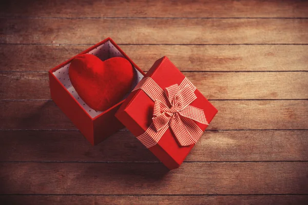 Red gift box with toy heart inside on wooden table. — Stock Photo, Image