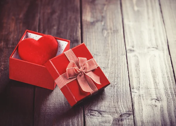 Red gift box with toy heart inside on wooden table. — Stock Photo, Image