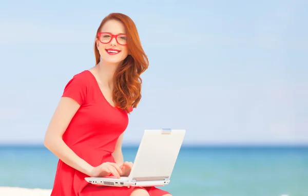 Fille rousse dans les lunettes avec ordinateur portable sur la plage — Photo