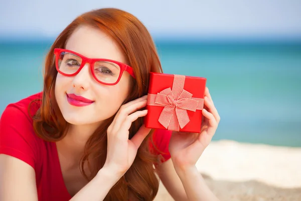 Rothaarige Mädchen in der Brille mit Geschenk am Strand — Stockfoto