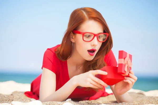 Rothaarige Mädchen in der Brille mit Geschenk am Strand — Stockfoto