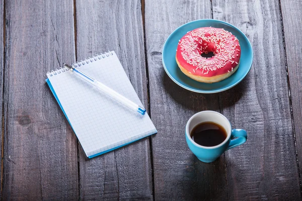 Чашка кофе с блокнотом и пончиком . — стоковое фото