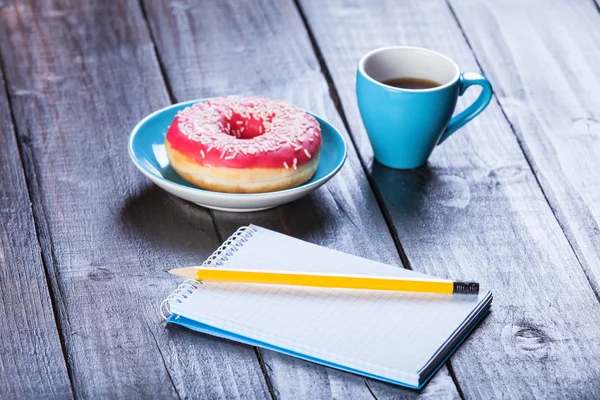 Cup of coffee with notebook and donut. — Stock Photo, Image