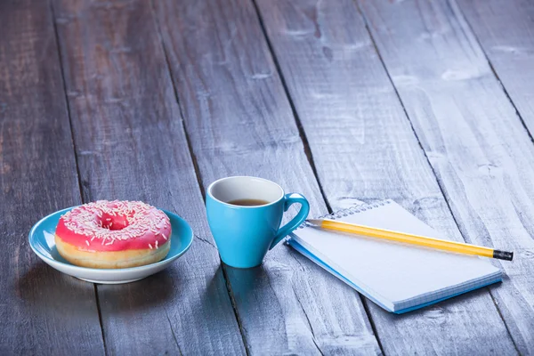 Kopje koffie met notebook en donut. — Stockfoto