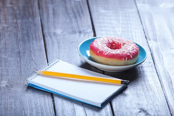 Notebook, donut and pencil on wooden table. — Stock Photo, Image