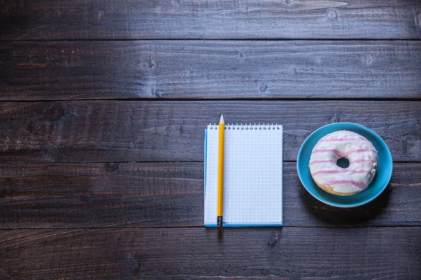 Quaderno, ciambella e matita su tavola di legno . — Foto Stock