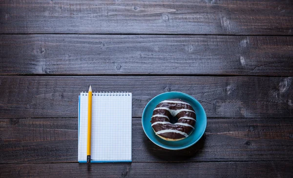 Notebook, donut and pencil on wooden table. — Stock Photo, Image