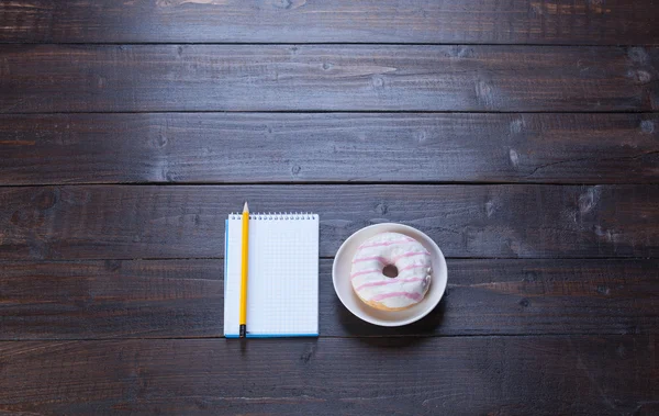 Notebook, donut en potlood op houten tafel. — Stockfoto