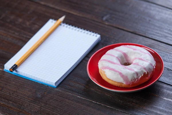 Carnet, beignet et crayon sur table en bois . — Photo