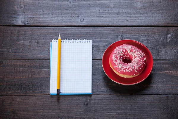 Notebook, donut en potlood op houten tafel. — Stockfoto