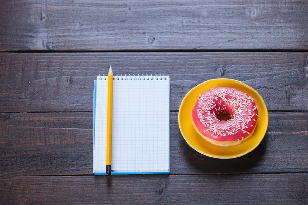 Notizbuch, Donut und Bleistift auf Holztisch. — Stockfoto