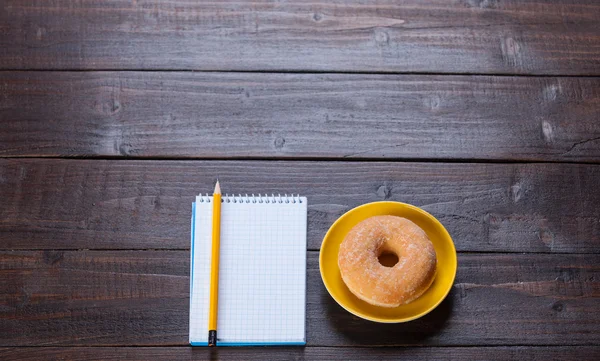 Notebook, donut and pencil on wooden table. — Stock Photo, Image