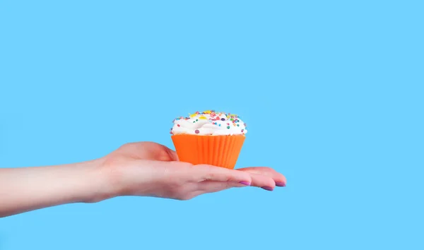 Mão segurando cupcake no fundo azul — Fotografia de Stock