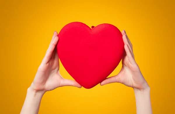 Händerna håller formen hjärta på gul bakgrund. — Stockfoto
