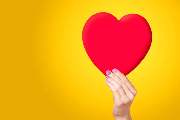 Mani che tengono forma cuore su sfondo giallo . — Foto Stock