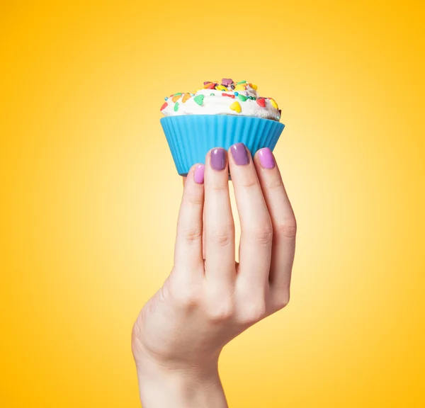 Hand holding cupcake on yellow background — Stock Photo, Image