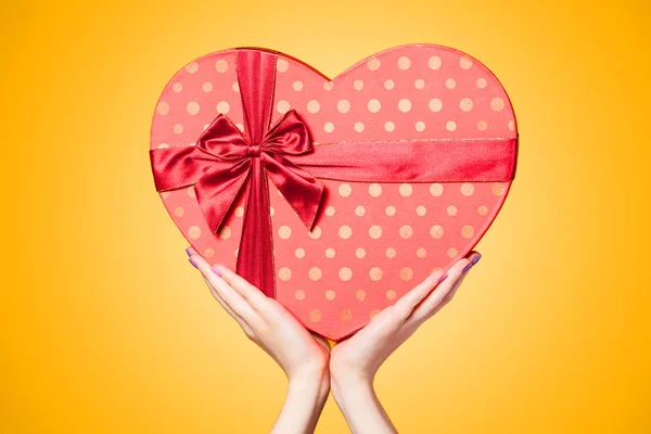 Hands holding shape heart box on yellow background. — Stock Photo, Image