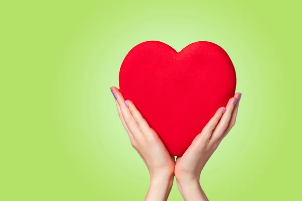 Händer som håller formen hjärta på grön bakgrund. — Stockfoto