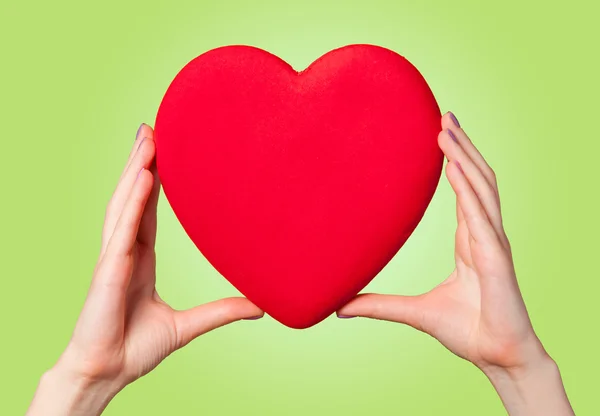 Manos sosteniendo la forma del corazón sobre fondo verde . — Foto de Stock