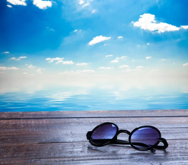 Sonnenbrille auf Holztisch und Meer im Hintergrund. — Stockfoto