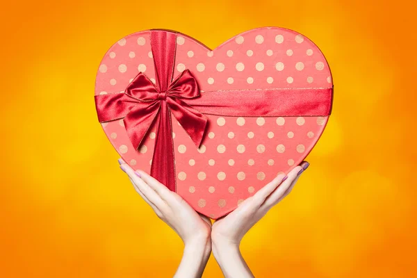 Hands holding shape heart box on yellow background. — Stock Photo, Image