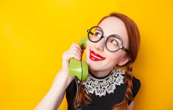 Roodharige meisje met groene telefoon op gele achtergrond. — Stockfoto